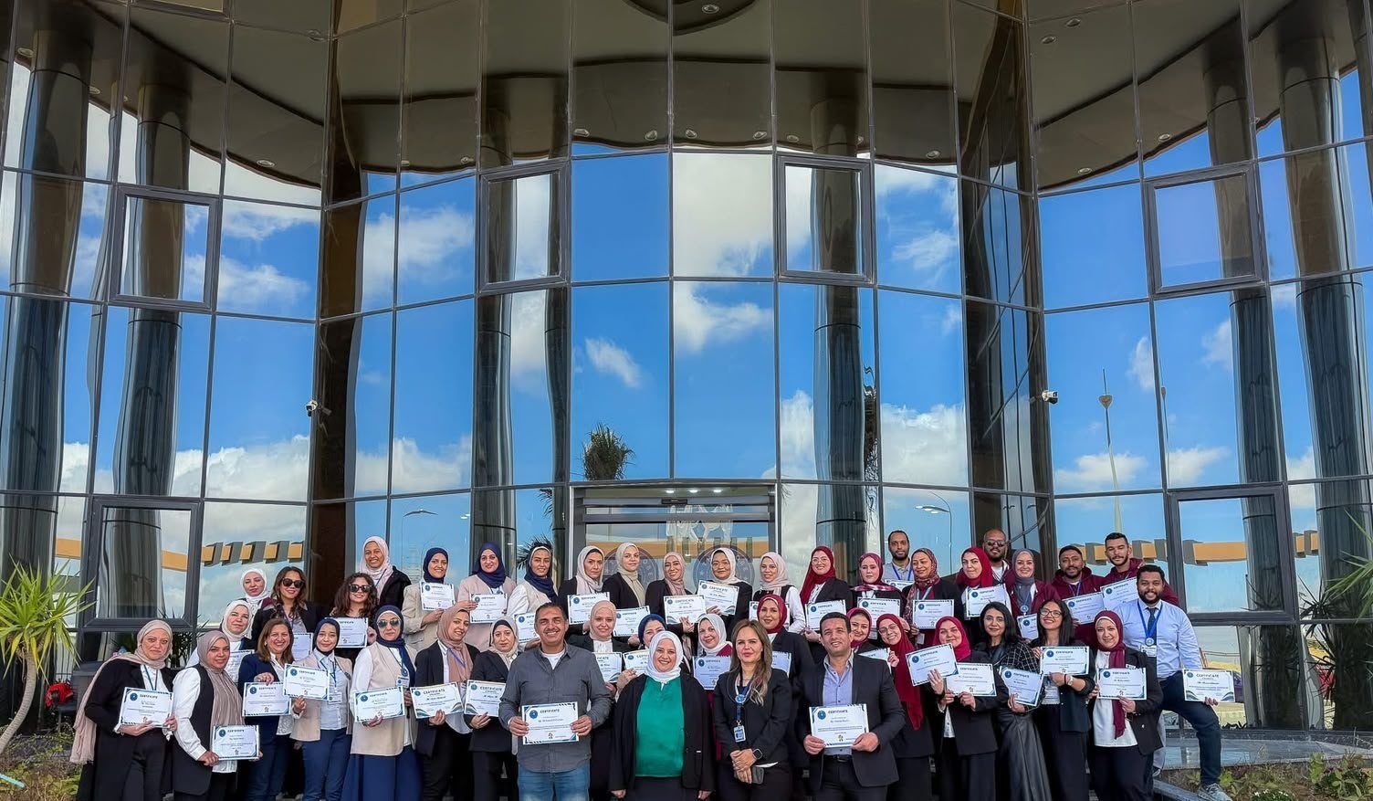 Teachers holding training certificates in front of the school